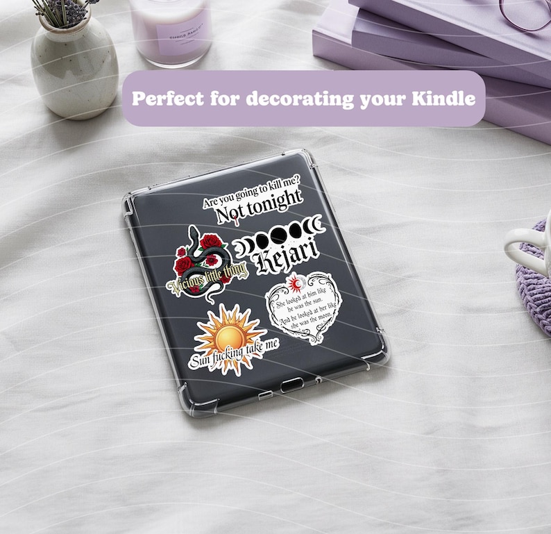 May include: A clear protective case for an e-reader, decorated with stickers. The stickers include phrases like "Are you going to kill me? Not tonight" and "Sun fucking take me." Other stickers feature a snake, roses, and a sun.