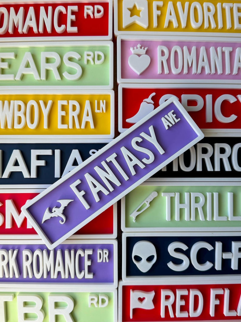 May include: A collection of colorful street signs with white raised lettering. The signs feature various themes like "Fantasy Ave," "Romance," and "Favorite." Each sign has a unique color and design, including a dragon and a heart.