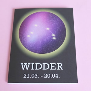 May include: A black card with the word "WIDDER" in white text, along with the dates 21.03. - 20.04. The card features a purple and white celestial design with a yellow outline. The background is a light pink.