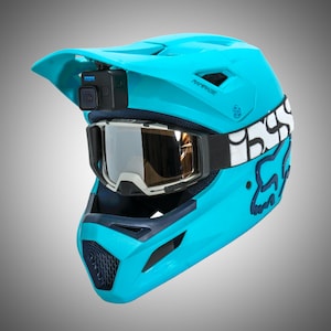 May include: A blue and black full-face helmet with a built-in camera and goggles. The helmet has a white and black Fox Racing logo on the side. The camera is mounted on the top of the helmet and has a black and blue design. The goggles are black and have a clear lens.