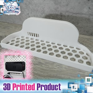 Puede incluir: Estante blanco impreso en 3D con base de panal y respaldo curvo. El estante está diseñado para sostener un dispositivo de juego. El texto "3D Printed Product" está en la parte inferior de la imagen.