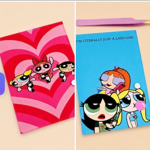 May include: Two notebooks with Powerpuff Girls designs. One has a red and pink heart pattern with the characters. The other is blue with the text "I'M LITERALLY JUST A LASH GIRL" and Powerpuff Girls characters. A pair of pink tweezers is also visible.
