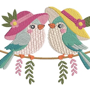 Könnte beinhalten: Gesticktes Design mit zwei Vögeln auf einem Ast. Jeder Vogel trägt einen Hut mit floralen Akzenten. Die Vögel haben blaue, rosa und gelbe Farben, mit grünen Blättern und rosa floralen Akzenten auf weißem Hintergrund.