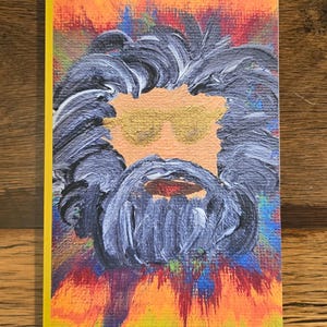 May include: A greeting card with a painted portrait of a person with a beard and sunglasses. The portrait is on a yellow-bordered card with a colorful abstract background of orange, red, blue, and yellow.