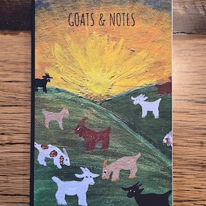 May include: A notebook with a colorful painted cover featuring a sunset and goats. The cover says "GOATS & NOTES".