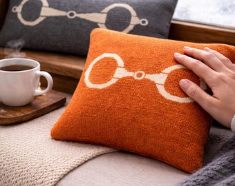 May include: Two decorative throw pillows with a horse bit design. One pillow is orange, the other is gray. The pillows are rectangular and have a textured appearance. A cup of coffee sits on a wooden tray next to the pillows.