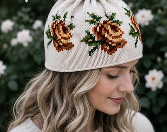 May include: Cream-colored knit hat with a drawstring closure and floral embroidery. The hat features brown, yellow, and green roses. The text "ANNA FLORIDA - TIMELESS BEAUTY" is printed on the hat. The hat is a winter accessory.