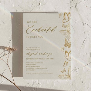 Pu&ograve; includere: Un invito color crema con scritte dorate e decorazioni a farfalla. Il testo recita "Siamo incantati di incontrarvi" e include i dettagli dell'evento per la celebrazione di Abigail Mackenzie. Su sfondo bianco strutturato.