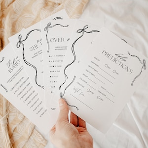 Puede incluir: Un conjunto de tarjetas blancas para juegos de baby shower con texto negro y dise&ntilde;os de lazo decorativos. Las tarjetas incluyen juegos como "El precio es correcto" y "Predicciones" con secciones para rellenar.