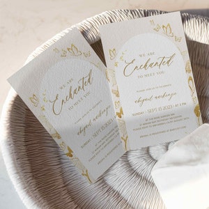 May include: Gold foil baby shower invitation with a butterfly design. The invitation reads "We are Enchanted to meet you" and includes the date, time, and location of the event. The text also says "Please join us to celebrate Abigail Mackenzie".
