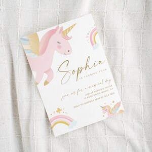 May include: A white invitation card featuring a pink unicorn with a golden horn and wings, a rainbow, and the name "Sophia" in gold script. The text reads "is turning four" and invites guests to a magical day.