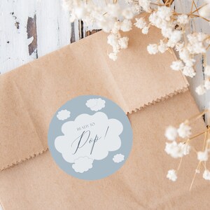 K&ouml;nnte beinhalten: Ein runder Aufkleber in Blau und Wei&szlig; mit dem Text "Ready to Pop!" in Form einer wei&szlig;en Wolke. Der Aufkleber befindet sich auf einem braunen Papierbeutel.