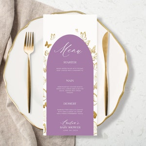 Puede incluir: Una tarjeta de men&uacute; p&uacute;rpura y blanca con detalles de mariposas doradas. La tarjeta de men&uacute; tiene un t&iacute;tulo que dice "Men&uacute;" y enumera los elementos del men&uacute; para un baby shower. El texto en la parte inferior de la tarjeta dice "Crelia's Baby Shower June 04 2021."