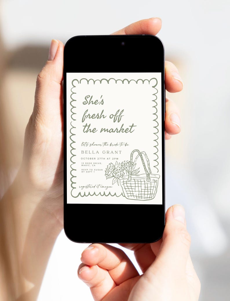 May include: A smartphone displays a bridal shower invitation with the text "She's fresh off the market." The invitation features a basket with flowers and text details in a decorative frame. The phone is held by two hands.