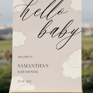 May include: A welcome sign for a baby shower with the text "hello baby" in a cursive font. The sign is beige with white clouds and the text "Welcome to Samantha's Baby Shower 25.06.2023".