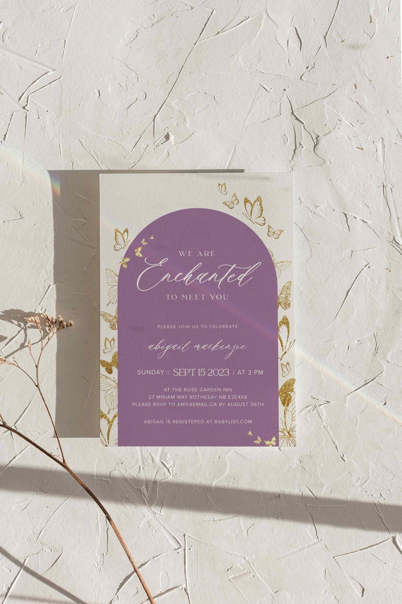 Puede incluir: Invitaci&oacute;n a la fiesta de bienvenida al beb&eacute; de color morado y dorado con tem&aacute;tica de mariposas. La invitaci&oacute;n dice "We are Enchanted to meet you" e incluye el nombre del beb&eacute;, la fecha, la hora y el lugar. Tambi&eacute;n se incluye informaci&oacute;n sobre la confirmaci&oacute;n de asistencia.