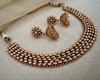 May include: A gold necklace with five rows of teardrop-shaped beads. The necklace is paired with matching earrings with a floral design.