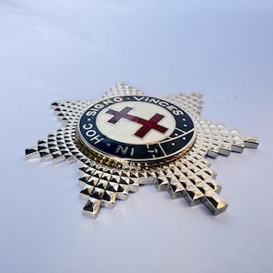 May include: A silver star-shaped badge with a red cross on a white circle surrounded by a blue ring with the text "HOC SIGNO VINCES IN NI" in black.