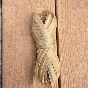 May include: A bundle of tan ribbon, tightly wound and tied in the middle, rests on a wooden surface. The ribbon has a velvety texture and a slight sheen. The wood planks are a warm brown color.