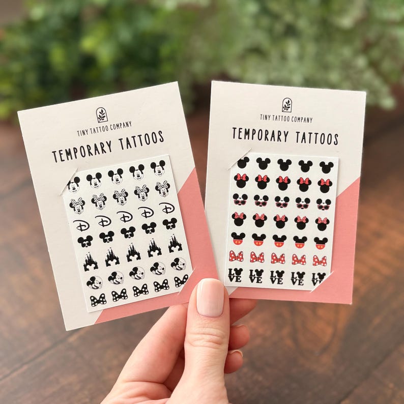 May include: Two white rectangular cards labeled Tiny Tattoo Company Temporary Tattoos. Each card holds a sheet of small black and colored temporary tattoos featuring various mouse head silhouettes, bows, castle icons, and the word LOVE in black.