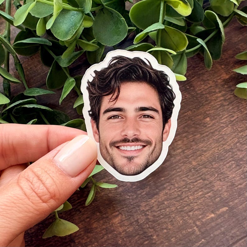 Puede incluir: Una pegatina troquelada que presenta un retrato realista y de alta resoluci&oacute;n de una persona con cabello casta&ntilde;o oscuro ondulado, ojos marrones y una barba corta y arreglada. El individuo sonr&iacute;e mostrando dientes blancos y tiene un borde blanco.