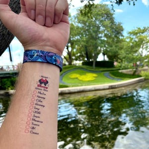 May include: A blue watch band featuring a repeating Stitch pattern and a temporary tattoo on the forearm. The tattoo displays the text Henry's Birthday World Tour with a Minnie Mouse icon and a checklist of countries including Mexico, Norway, China, Germany, Italy, USA, Japan, Morocco, France, UK, and Canada.