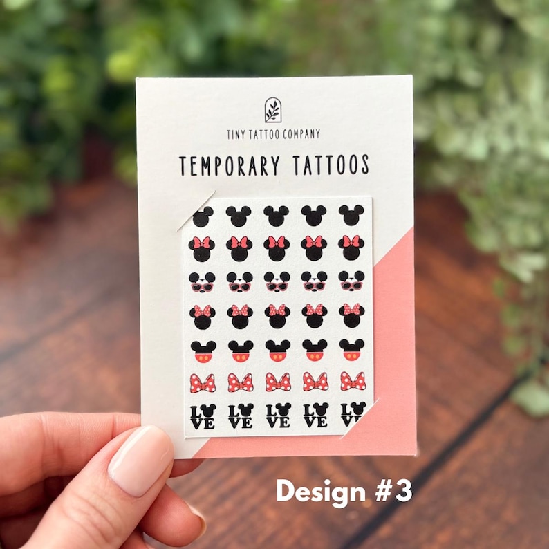 May include: A white card labeled Tiny Tattoo Company Temporary Tattoos featuring a grid of small black Mickey Mouse head icons, some with pink bows, pink sunglasses, or red shorts, and the word LOVE with Mickey ears, all arranged in six rows.
