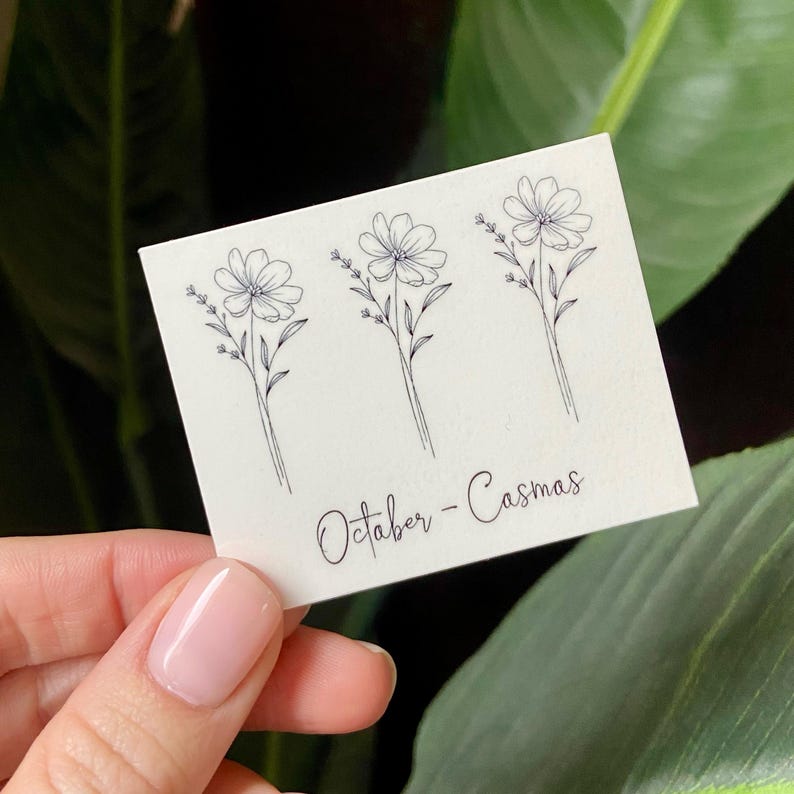 May include: Three simple line drawings of cosmos flowers on a white card with the text "October - Cosmos".