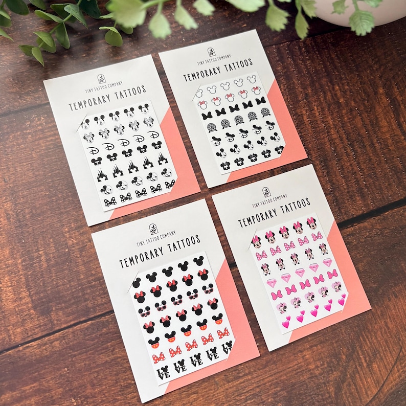 May include: Four white rectangular cards labeled Tiny Tattoo Company Temporary Tattoos, each featuring a grid of small black, pink, and red adhesive designs including mouse ears, bows, castles, diamonds, hearts, and the word love in various styles.