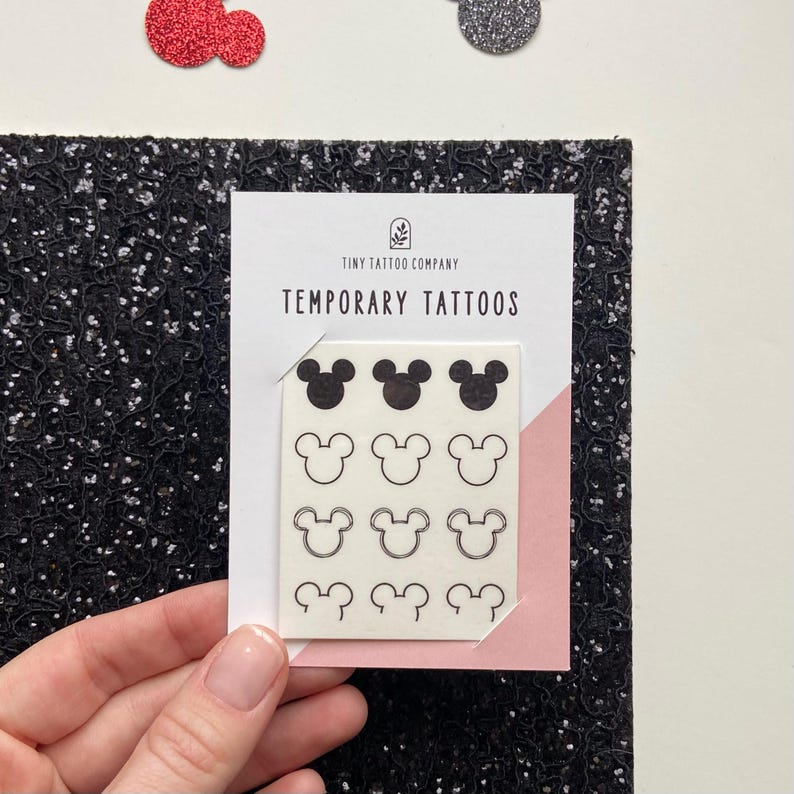 May include: A white rectangular card labelled Tiny Tattoo Company Temporary Tattoos featuring twelve black Mickey Mouse head icons arranged in four rows. The top row shows solid black silhouettes, while the remaining rows display various line art outlines.