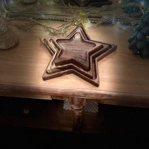 May include: A set of three wooden star-shaped trays, nested together. The trays are made of dark wood with a natural grain pattern. The trays are arranged on a wooden table.