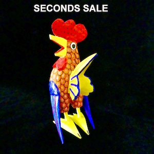 May include: A colorful wooden rooster figurine with a red comb, yellow beak, orange and yellow body, blue and yellow wings, and yellow feet. The rooster is painted with a detailed pattern of scales.