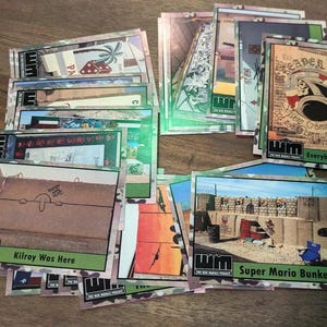 May include: A collection of trading cards featuring various illustrations and text. The cards have a camouflage border and include phrases like "Kilroy Was Here" and "Super Mario Bunkers." Some cards display images of bunkers and other scenes.