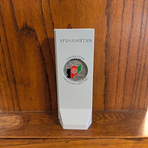 May include: A gray rectangular plaque with the text "AFGHANISTAN" and "OPERATION FREEDOM'S SENTINEL" with a silver coin featuring a map of Afghanistan with the Afghan flag.
