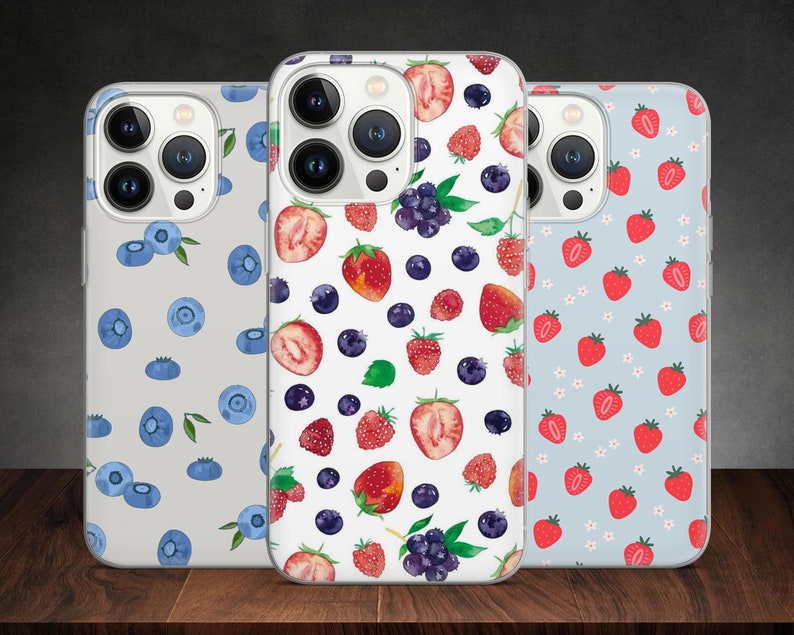 Puede incluir: Tres fundas transparentes para tel&eacute;fono con diferentes dise&ntilde;os. La primera funda tiene un fondo blanco con ar&aacute;ndanos azules y hojas verdes. La segunda funda tiene un fondo blanco con fresas rojas, ar&aacute;ndanos y moras. La tercera funda tiene un fondo azul claro con fresas rojas y flores blancas.