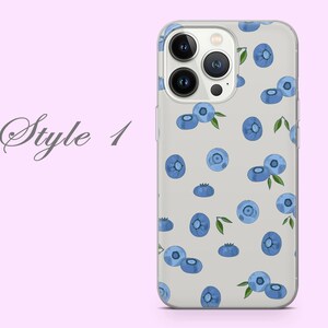 Puede incluir: Una funda transparente para tel&eacute;fono con un patr&oacute;n de ar&aacute;ndanos azules sobre un fondo blanco. La funda est&aacute; dise&ntilde;ada para un iPhone con una lente de c&aacute;mara triple.