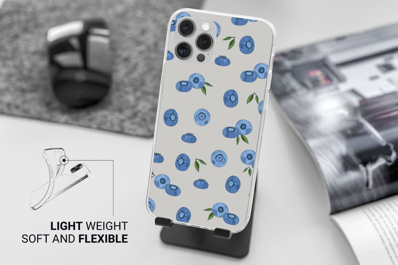 Puede incluir: Una funda transparente para tel&eacute;fono con fondo blanco y un patr&oacute;n de ar&aacute;ndanos azules. La funda est&aacute; dise&ntilde;ada para un tel&eacute;fono con una protuberancia de c&aacute;mara y tiene un dise&ntilde;o ligero y flexible.