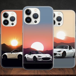 Puede incluir: Tres fundas transparentes para teléfono con un diseño de puesta de sol y un coche deportivo blanco. Las fundas son para un iPhone con una protuberancia de cámara.