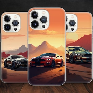 以下が含まれることがあります： 砂漠の風景を背景にした、フォード・マスタングが描かれたiPhoneケースが3つ。左側のケースのマスタングは黒、中央のケースのマスタングは赤、右側のケースのマスタングは銀色です。