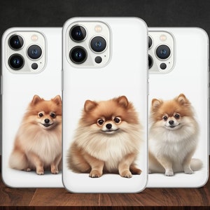 Puede incluir: Tres fundas blancas para iPhone con un perro Pomerania esponjoso en cada funda. Los perros están todos sentados y mirando a la cámara. Las fundas son de diferentes colores.
