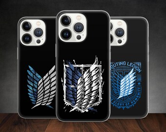 Może przedstawiać: Trzy czarne etui na iPhone'a z różnymi wzorami przedstawiającymi Skrzydła Wolności z anime Atak Tytanów. Etui po lewej stronie ma srebrny i niebieski wzór skrzydeł. Etui pośrodku ma biały i niebieski wzór skrzydeł na czarno-białym tle. Etui po prawej stronie ma niebieski i biały wzór skrzydeł z tekstem "Scouting Legion" i "For the Glory of Humanity".