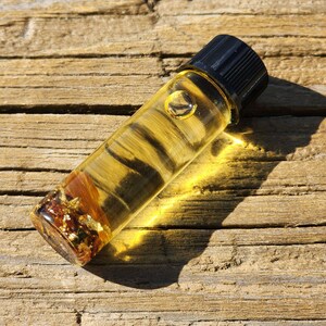 May include: A small glass bottle filled with a clear liquid and gold flakes. The bottle has a black cap and is sitting on a wooden surface.