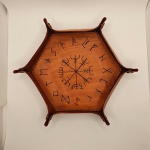 Puede incluir: Una bandeja hexagonal de cuero marrón con un diseño de rosa de los vientos y runas alrededor del borde.