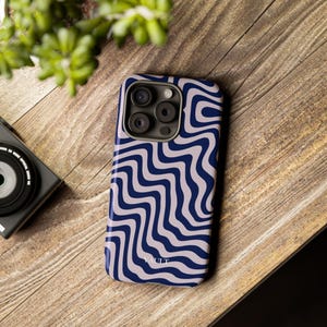 Può includere: Custodia per smartphone con un motivo a onde blu e bianco. La custodia ha una finitura lucida e copre la parte posteriore e i lati del telefono. La parola "VAULT" è stampata sul fondo della custodia. La custodia è su una superficie di legno.