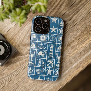 Può includere: Una custodia per smartphone blu con un motivo a griglia di icone nautiche bianche, tra cui fari, ancore, barche a vela, stelle marine, tartarughe marine, aragoste, polpi e bussole. La custodia presenta un ritaglio per il sistema a tripla fotocamera.