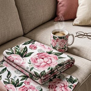 Può includere: Un set di articoli per l'arredamento della casa a tema floreale, tra cui una coperta, un sottobicchiere e una tazza da caffè. Gli articoli presentano peonie rosa e foglie verdi su sfondo bianco. La tazza contiene caffè.