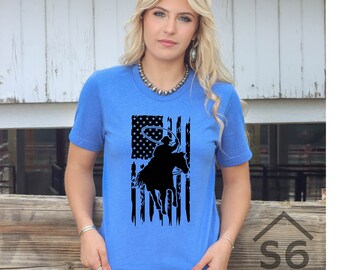 May include: A royal blue t-shirt with a distressed American flag design featuring a silhouette of a cowboy riding a horse and lassoing.