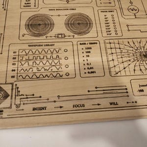 May include: A wooden panel with etched diagrams and text, including "Wave Induction Coil," "Waveform Library," and "Rain/Tempo." The design features geometric shapes, lines, and a balance scale, with the words "Intent," "Focus," and "Will" displayed.