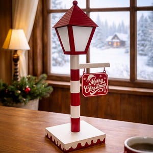May include: A decorative Christmas lamp post with a red and white striped pole, a red roof, and a sign that reads "Merry Christmas." The lamp post is on a white base with a red trim. A red mug of coffee sits on a wooden table.