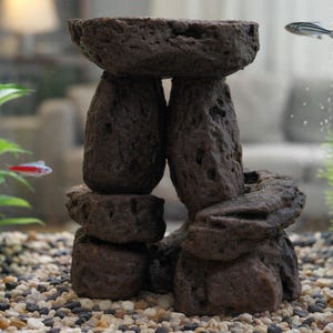 Può includere: Decorazione per acquario marrone scuro a forma di struttura in pietra, con una parte superiore piatta sostenuta da due pilastri e pietre più piccole. L'acquario contiene ghiaia, piante e piccoli pesci. L'acqua è limpida.